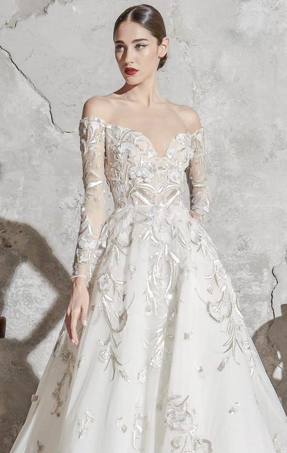 Длинное, пышное свадебное платье А-силуэта от Zuhair Murad. Подол декорирован цветочными элементами, которые имеются также на бюстье и полуспущенных длинных рукавах. Коллекция 2020