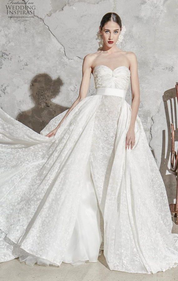 Белое пышное свадебное платье Flora от мастеров ателье Zuhair Murad адресовано стройным девушкам, желающим подчеркнуть изящность талии и красоту плечей. Модель из фактурной глянцевой ткани не имеет рукавов, поэтому для торжества, проходящего в холодное время года, следует заранее приготовить меховое манто или палантин. Пышный подол увеличен в объемах на боках за счет дополнительных съемных элементов. Атласный пояс придает образу аристократичности. Zuhair Murad Bridal Spring 2020 Collection
